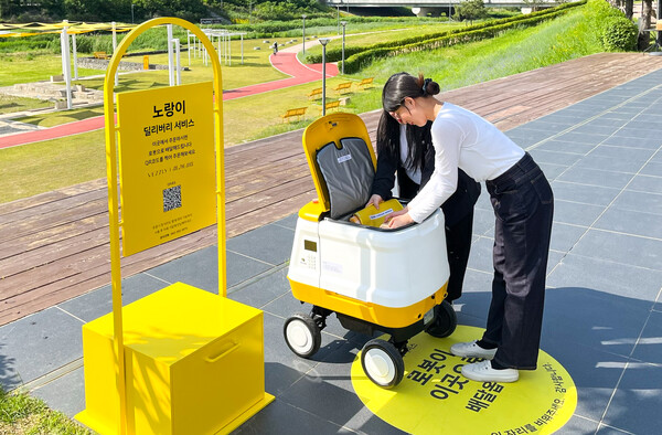 20일 오전 대전 유성구에 위치한 현대프리미엄아울렛 대전점 야외 생태공원 옐로우 스프링스 입구에서 고객들이 딜리버리 로봇 '노랑이'가 배달한 음식을 꺼내고 있다/사진제공=현대백화점